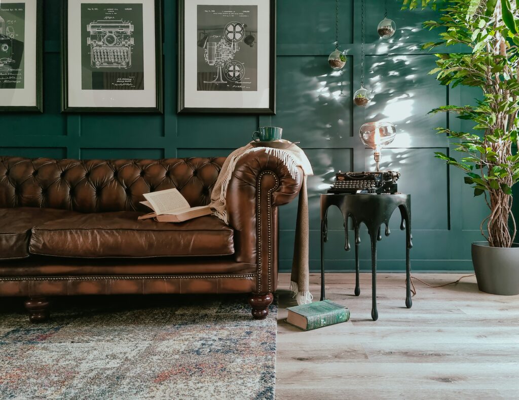 A vintage stílusú otthon hangulatát egy barna chesterfield bőrkanapé, zöld falipanelek, bekeretezett retró grafikák, üveg függődíszek és egy írógéppel díszített kis asztal adja.